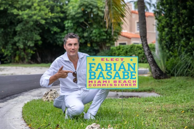 Fabian Basabe poses for photo on a lawn next to a campaign sign
