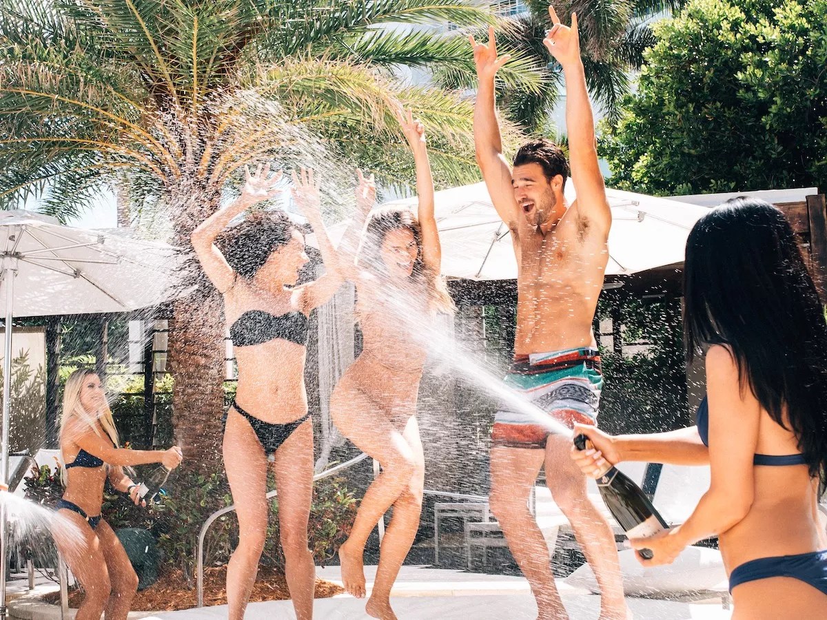 three people dance as someone sprays champagne on them