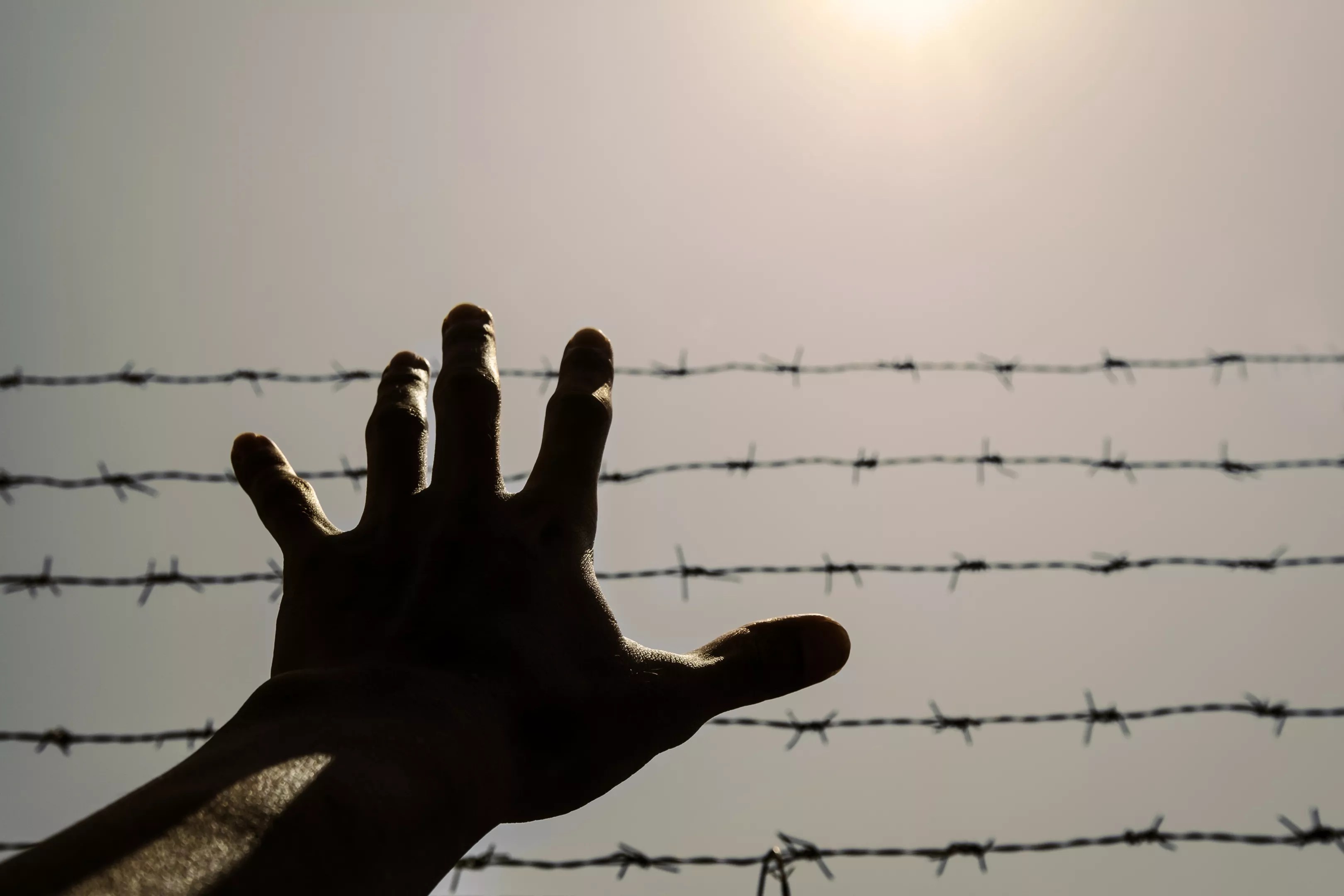 A hand reaching before a barbed wire fence