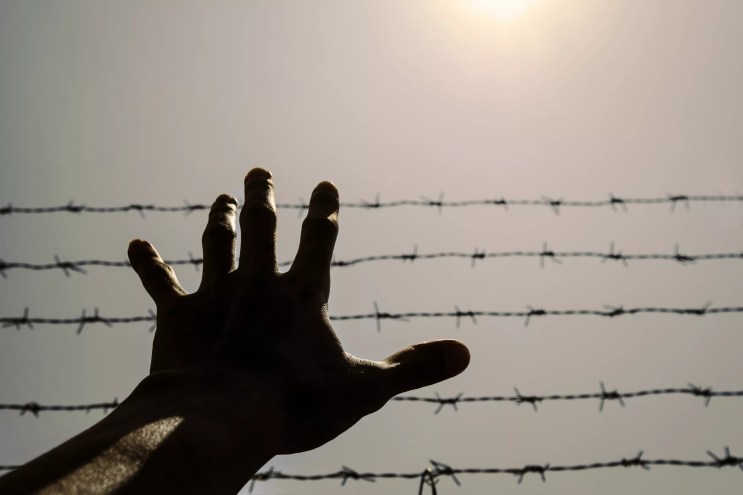 A hand reaching before a barbed wire fence