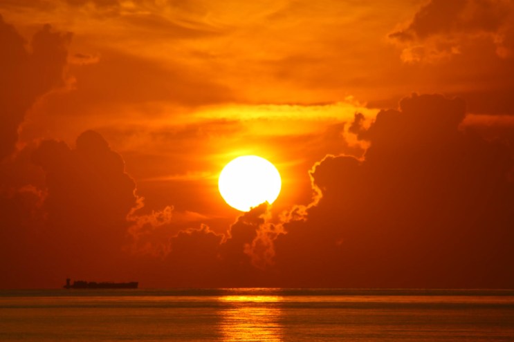 A large orange sun glows above a body of water.