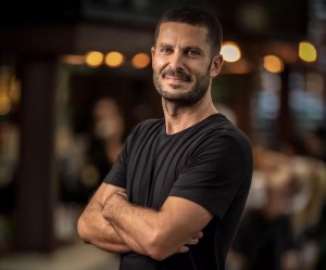 A headshot of Miami restaurateur Coco Coig wearing a black shirt taken at a restaurant.