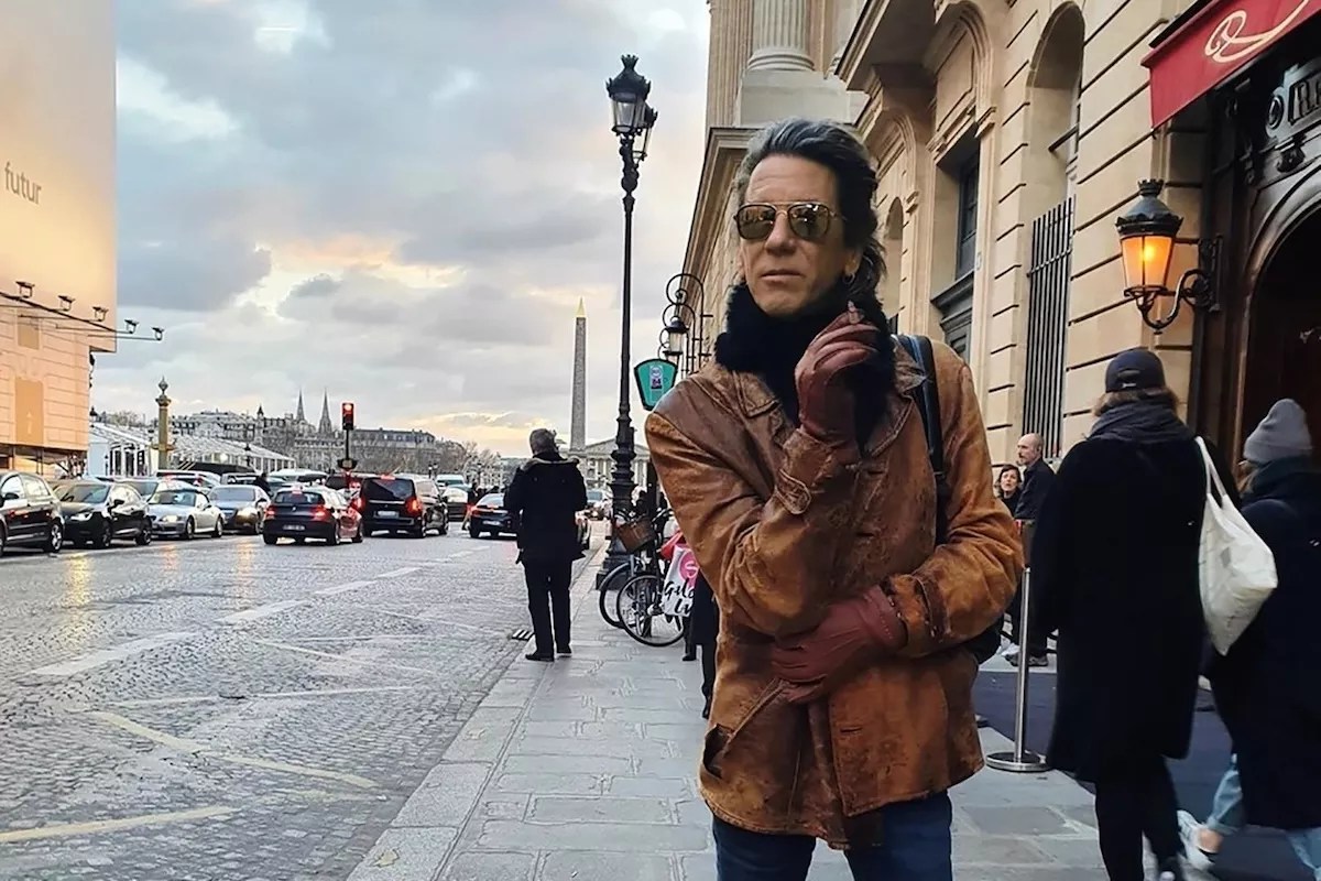 Composer William Basinski standing on the sidewalk smoking a cigarette