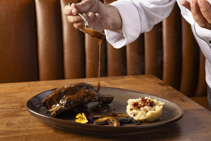 A chef pours sauce on steak
