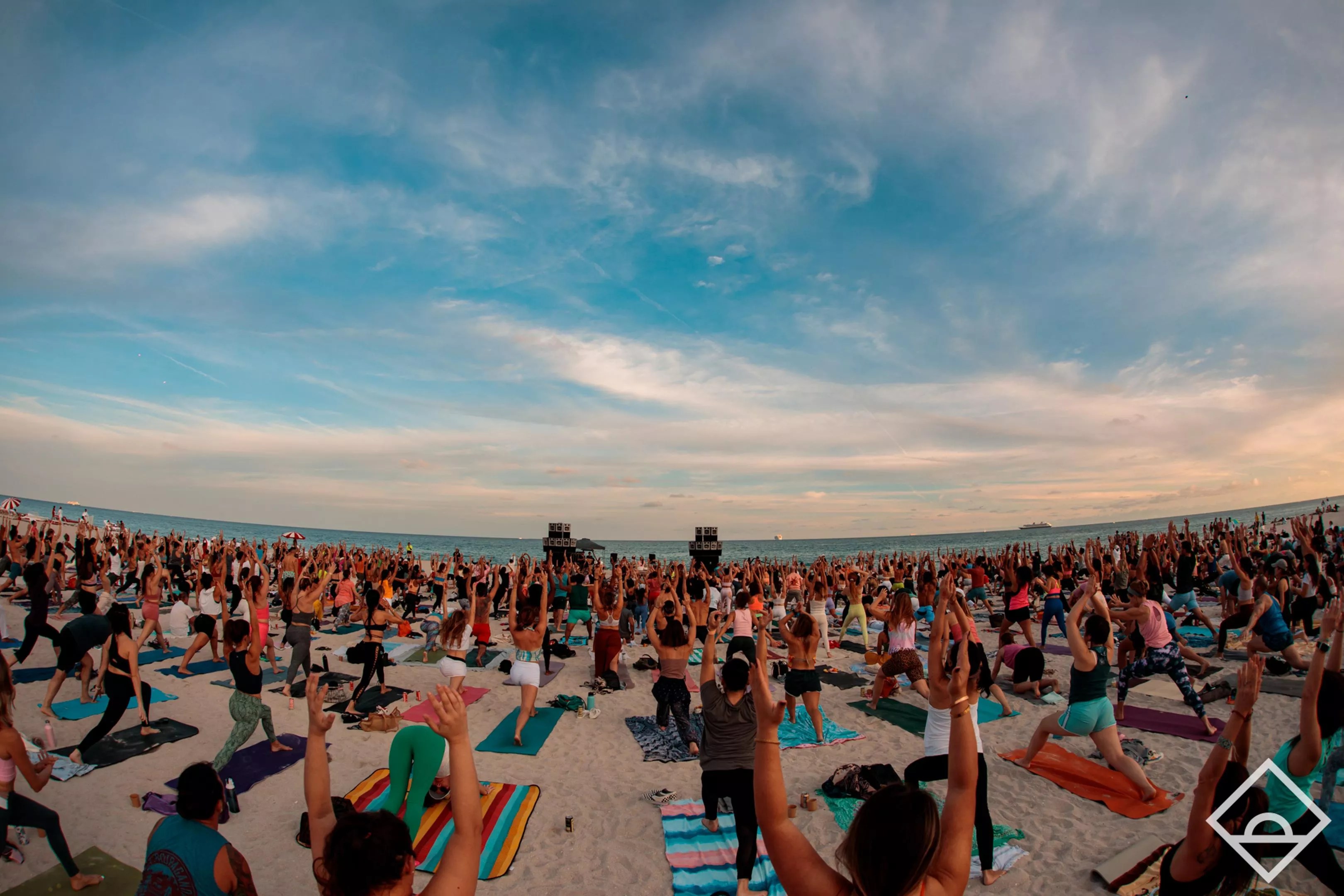 A large group of people doing yoga on the beach at dawn