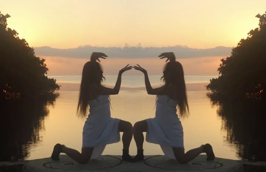 Still image from Caracoles en Cemento of a woman mirrored as she kneels with a sunset behind her