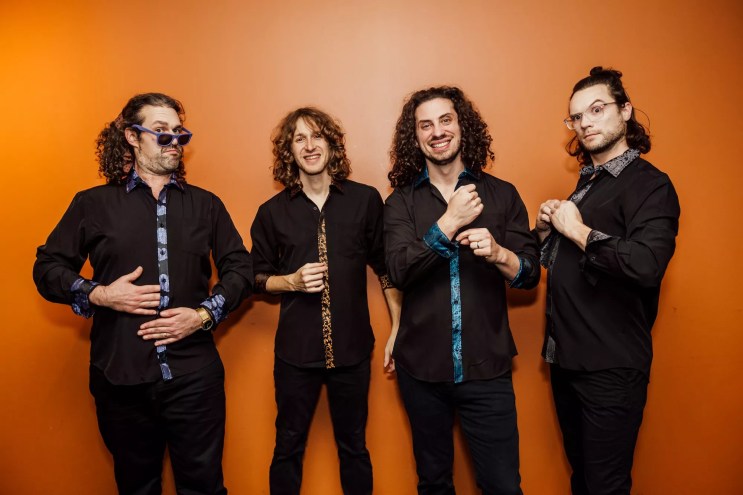 The four members of Pigeons Playing Ping Pong against a bright orange wall