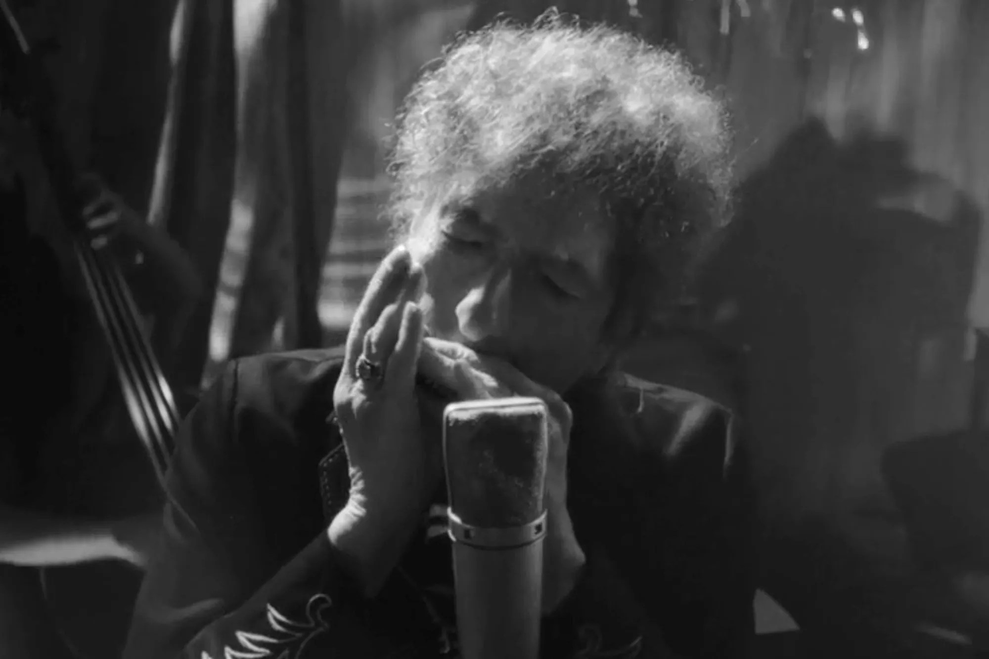 Bob Dylan playing the harmonica in front of a microphone