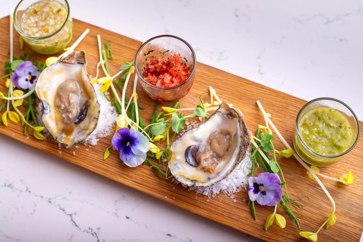 A platter of oysters and herbs on a wooden cutting board.