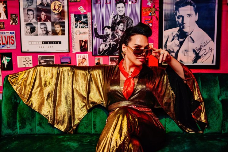 June Rave Romero seated on a couch in a gold jumpsuit and sunglasses