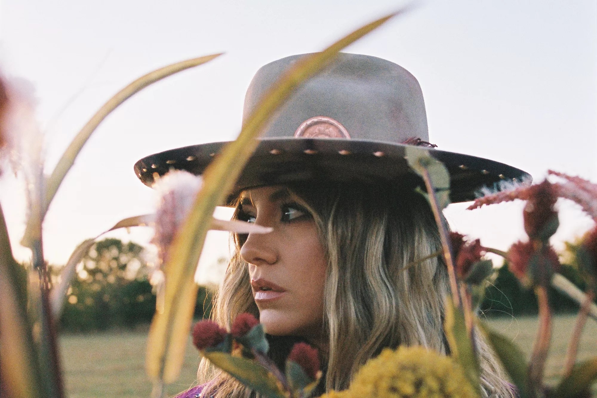 Portrait of Lainey Wilson partially obscured by cattail plants