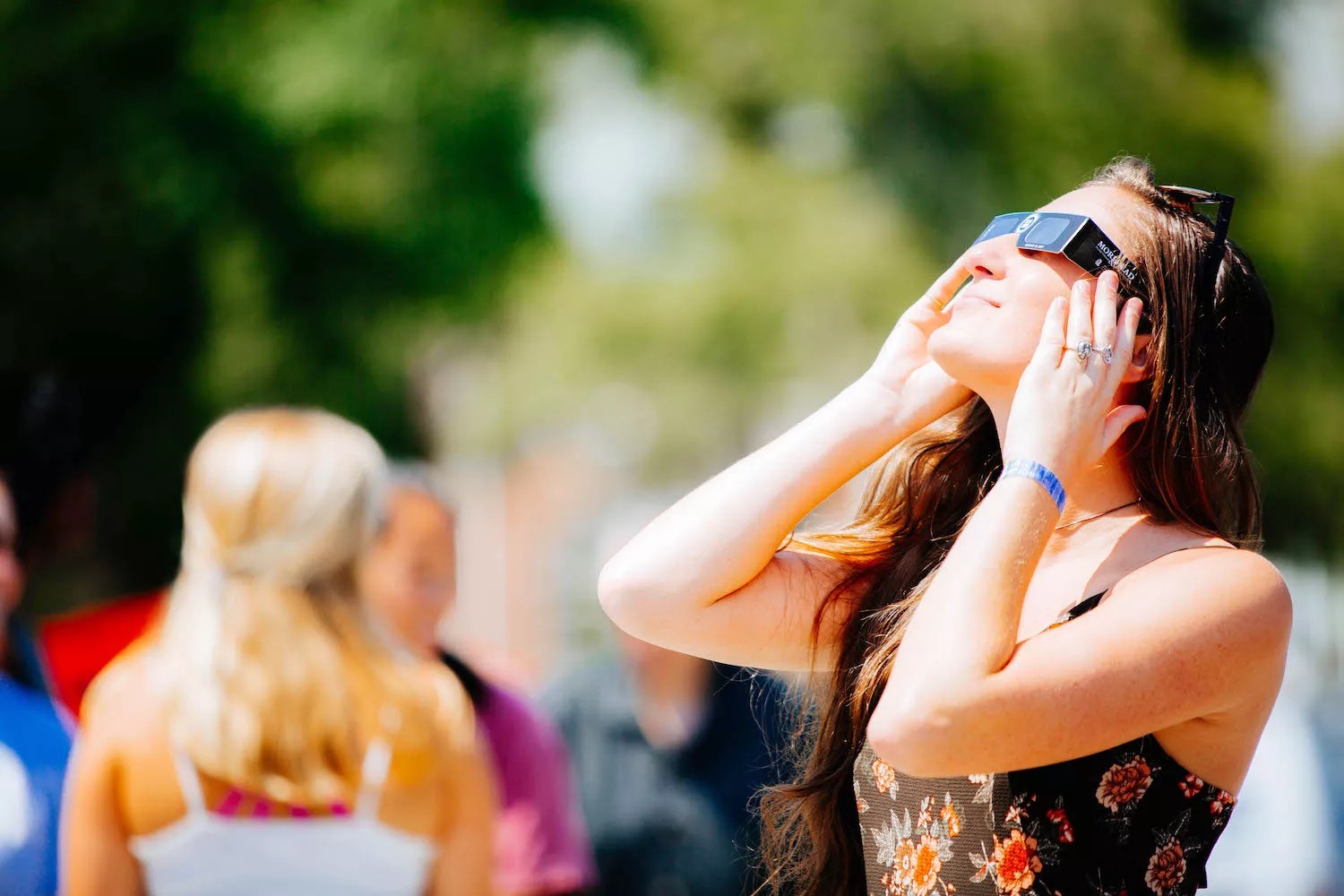 Color photo of  a young woman looks skyward during a solar eclipse while wearing the approved type of disposable eye protection
