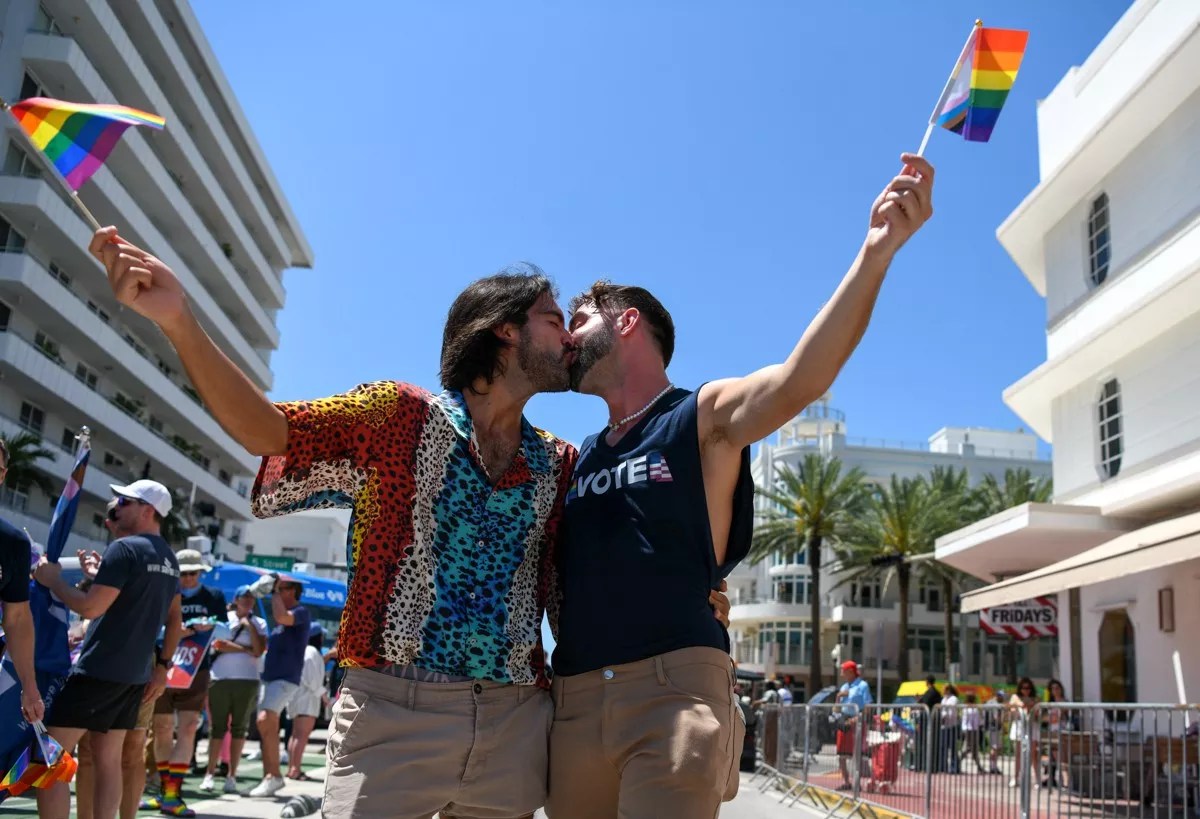 Two men kissing while holding gay pride flags