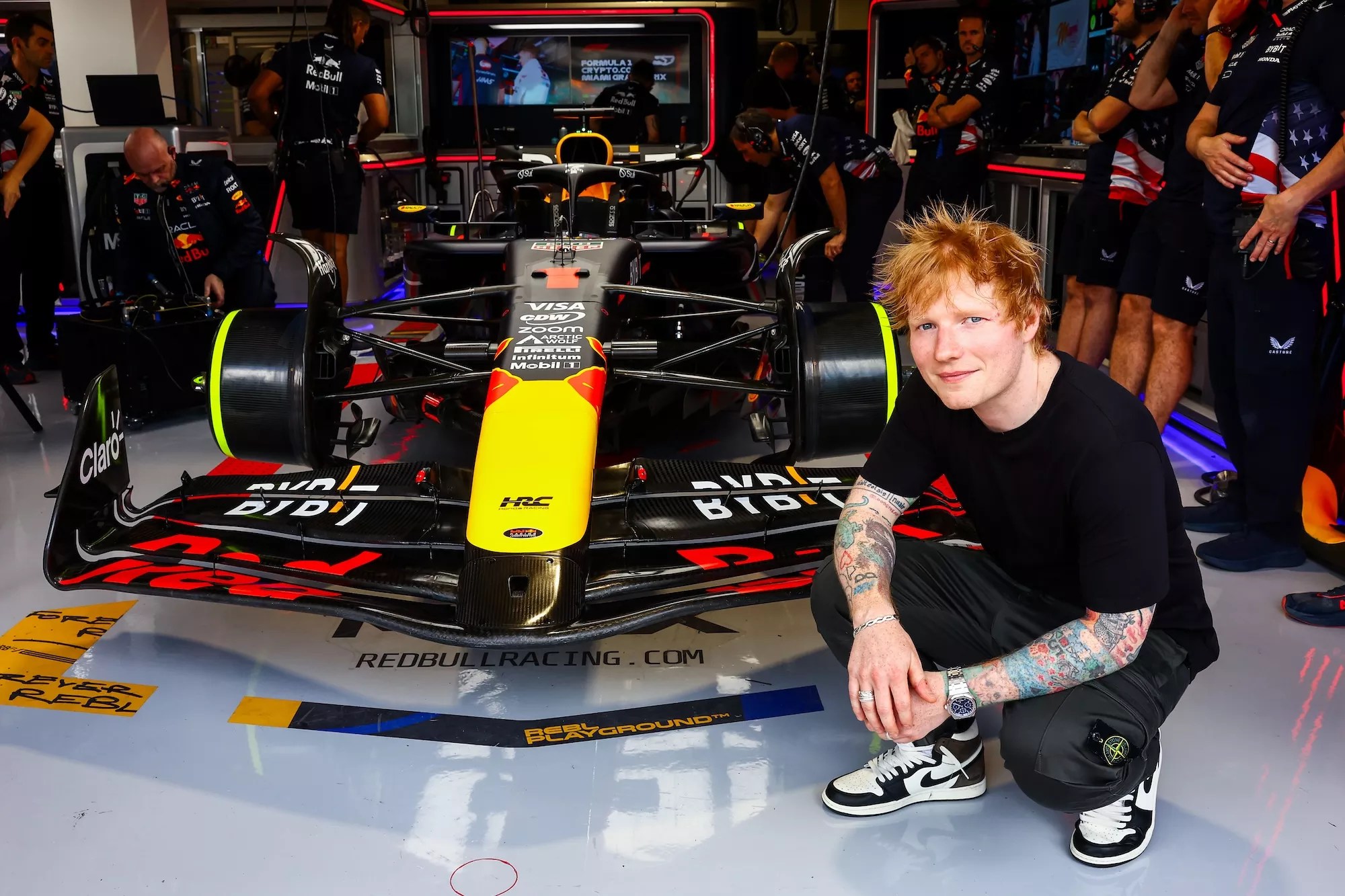 Ed Sheeran crouching down next to a race car