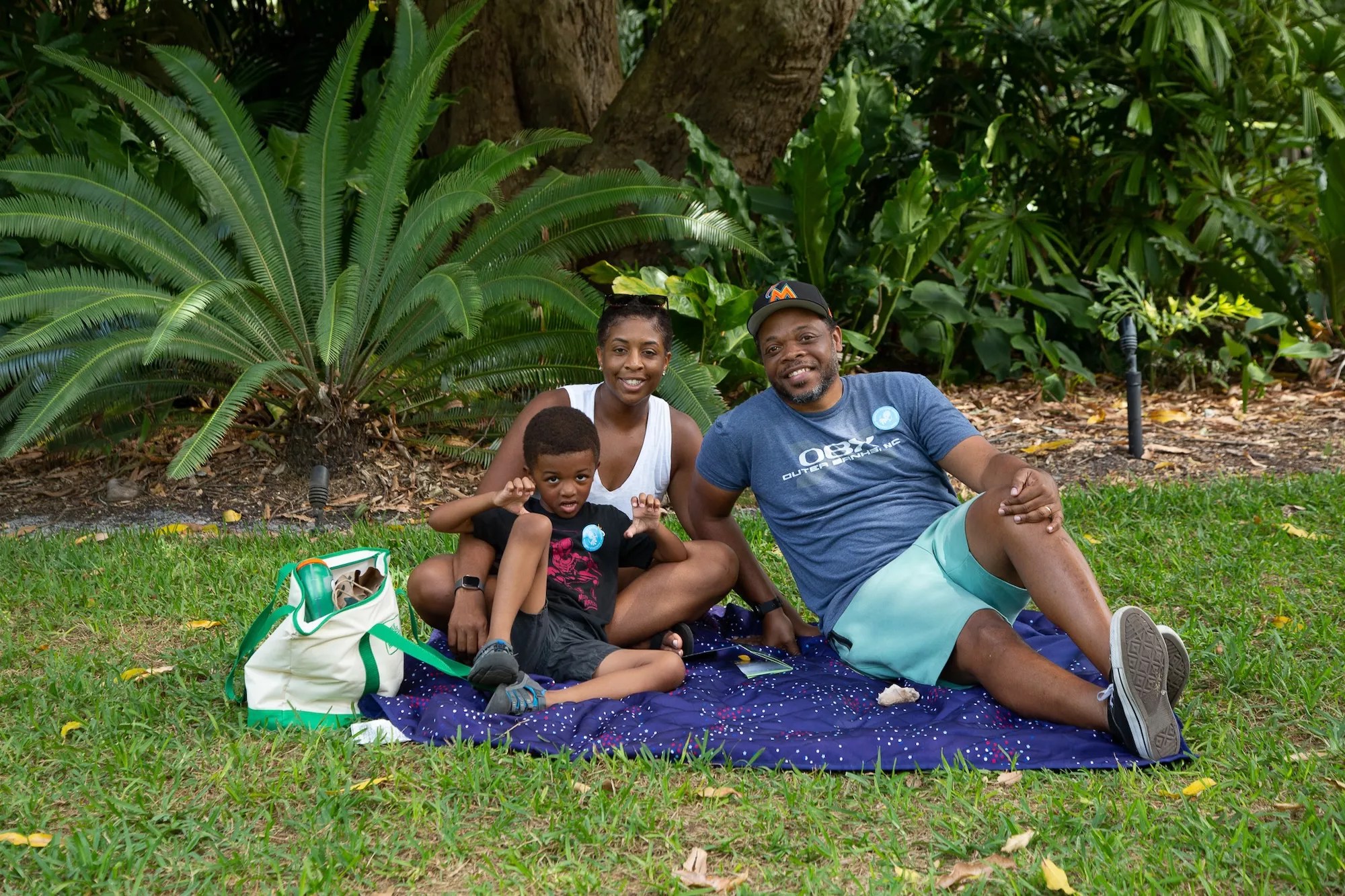 A mother and father with their child sitting on a picnic blanket at Fairchild Tropical Botanic Garden