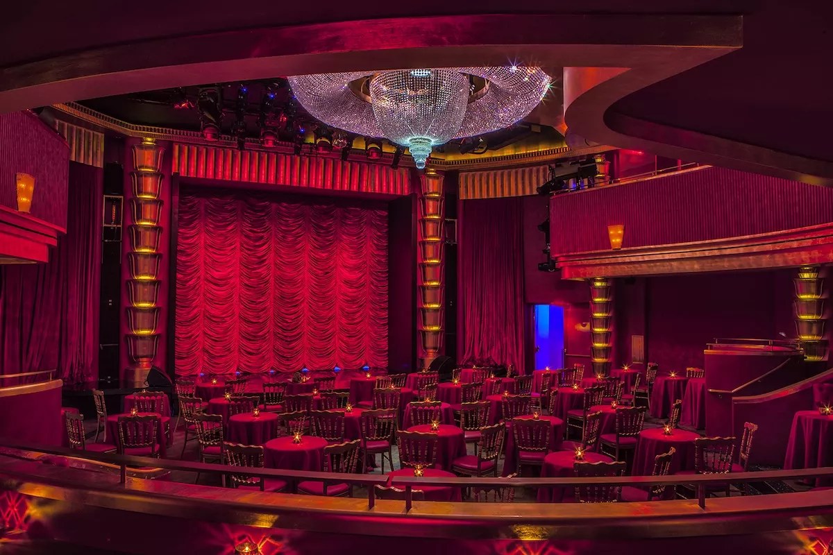 The interior of the Faena Theater with a red velvet curtain and huge crystal chandelier