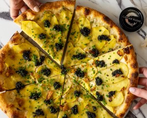 White pizza topped with caviar and a hand pulling it