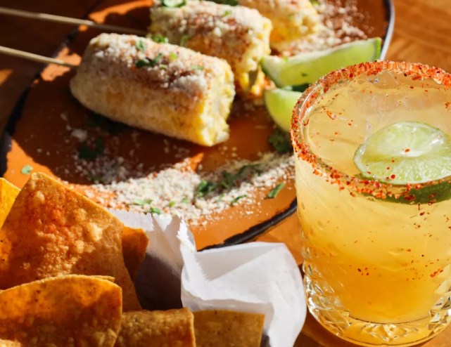 A cocktail and elotes corn on a table