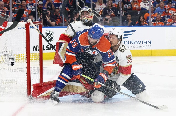 A Panthers player ties up an Edmonton Oilers skater at the Panthers net in the Stanley Cup Finals as ice sprays into the air