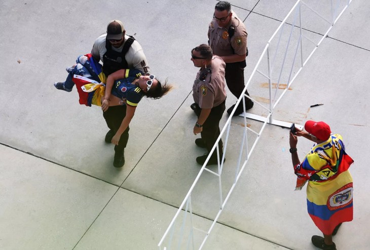 uniformed police officer carrying a seemingly unconscious soccer outside a large sports stadium