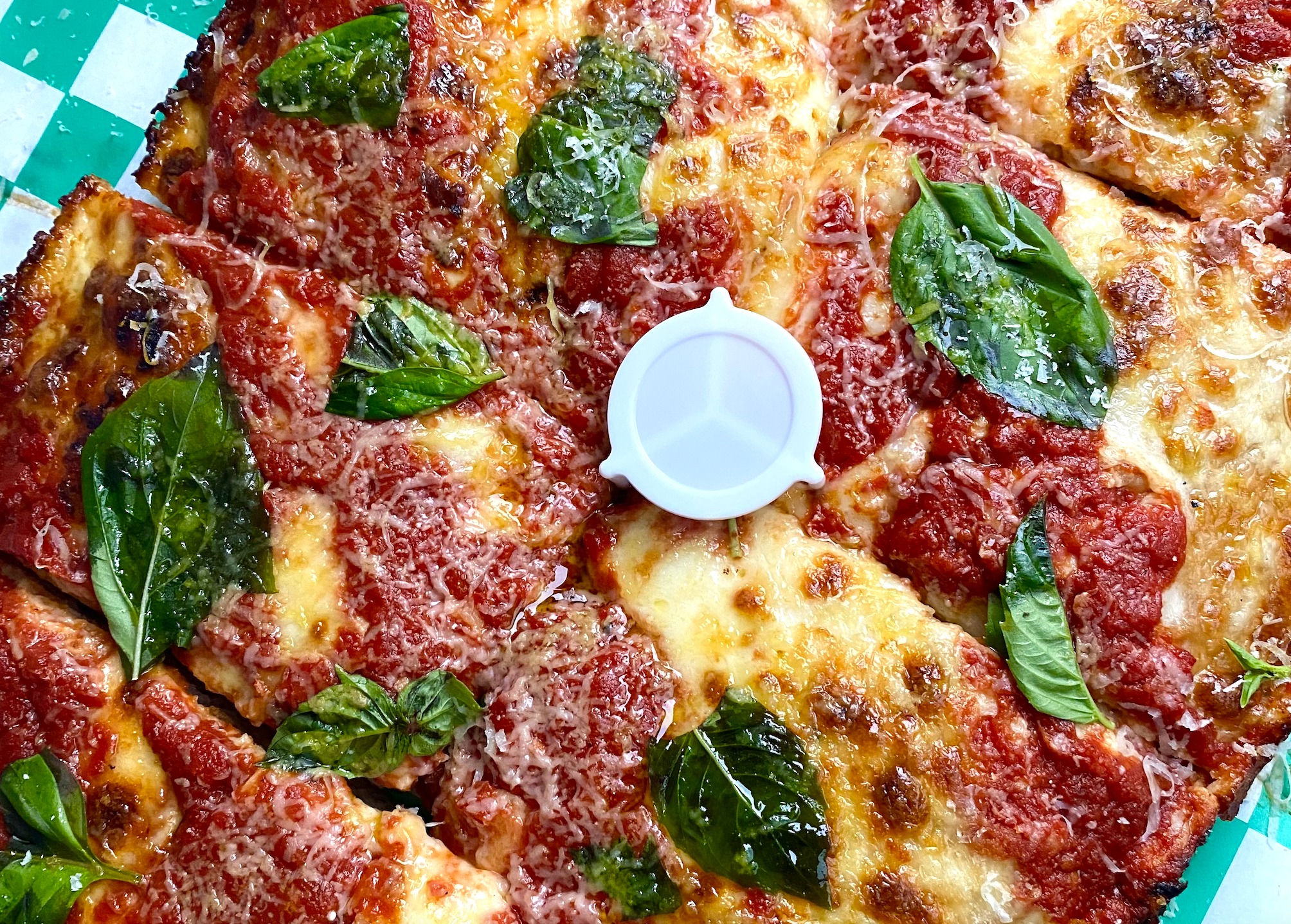 A close-up photo of a pizza from Old Greg's Pizza covered in cheese and basil