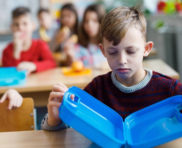 A downtrodden child stares at an empty lunchbox