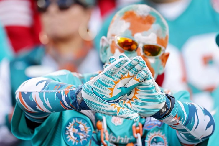 NFL football fan decked out in Miami Dolphins regalia, right down to his gloves and painted bald head