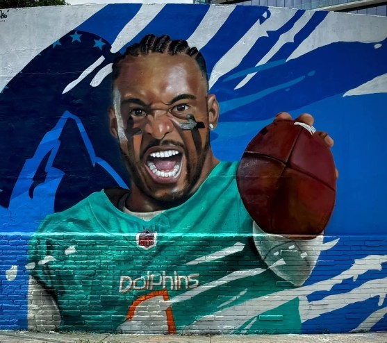 The finished mural of Tua Tagovailoa. He is wearing two black crosses in eyeblack, his mouth is wide open, and he is holding a football.