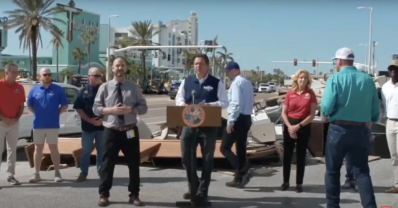 Ron DeSantis stands in front of a trash pile during a press conference.