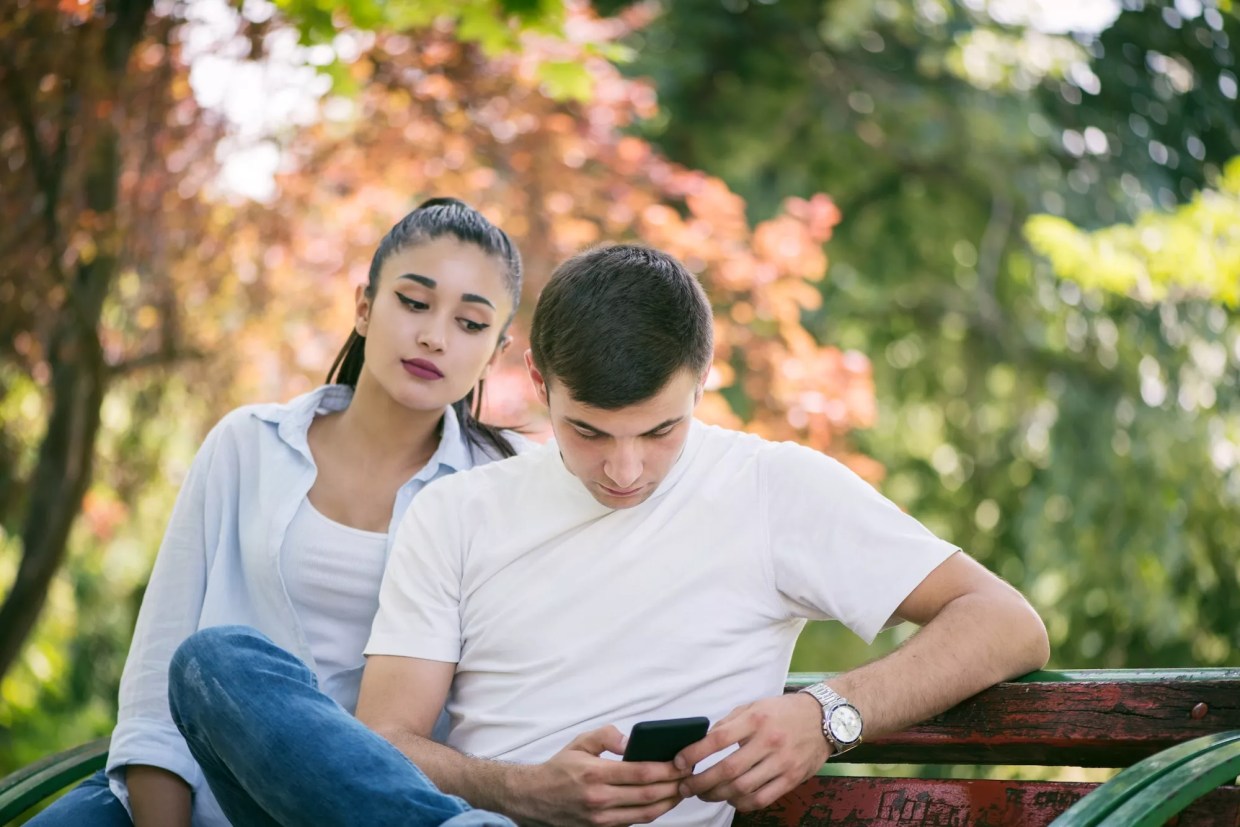 A woman looking over a man's shoulder at his phone