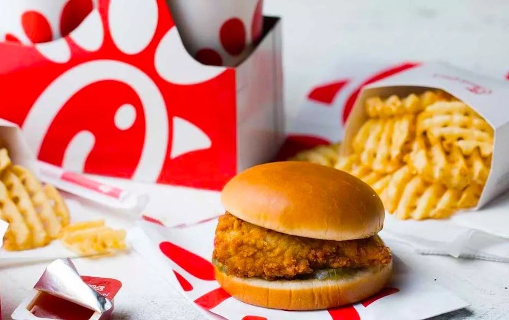 a fried chicken sandwich next to a cup of soda
