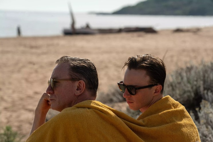 two men sit side by side wearing a yellow blanket over their shoulders