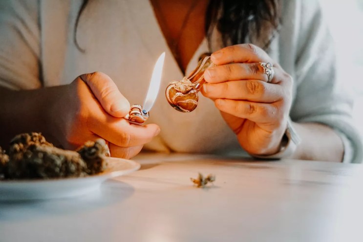 closeup of a woman preparing to light a glass pipe filled with marijuana flower
