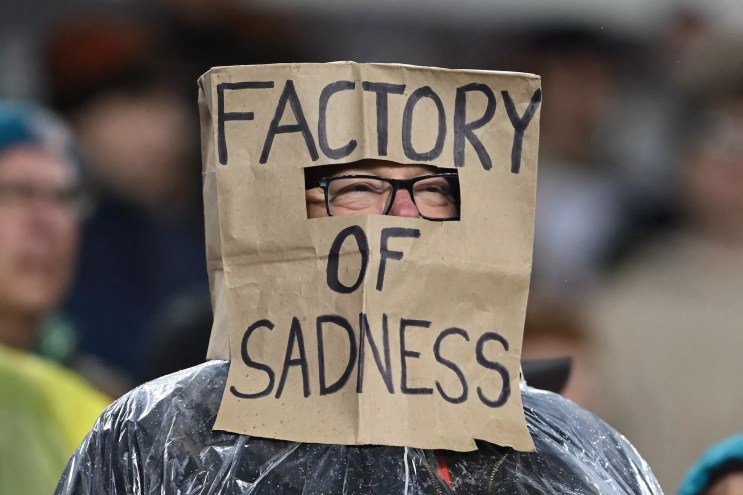 football fan with brown paper bag on head that says "FACTORY OF SADNESS," written in all caps with a Sharpie