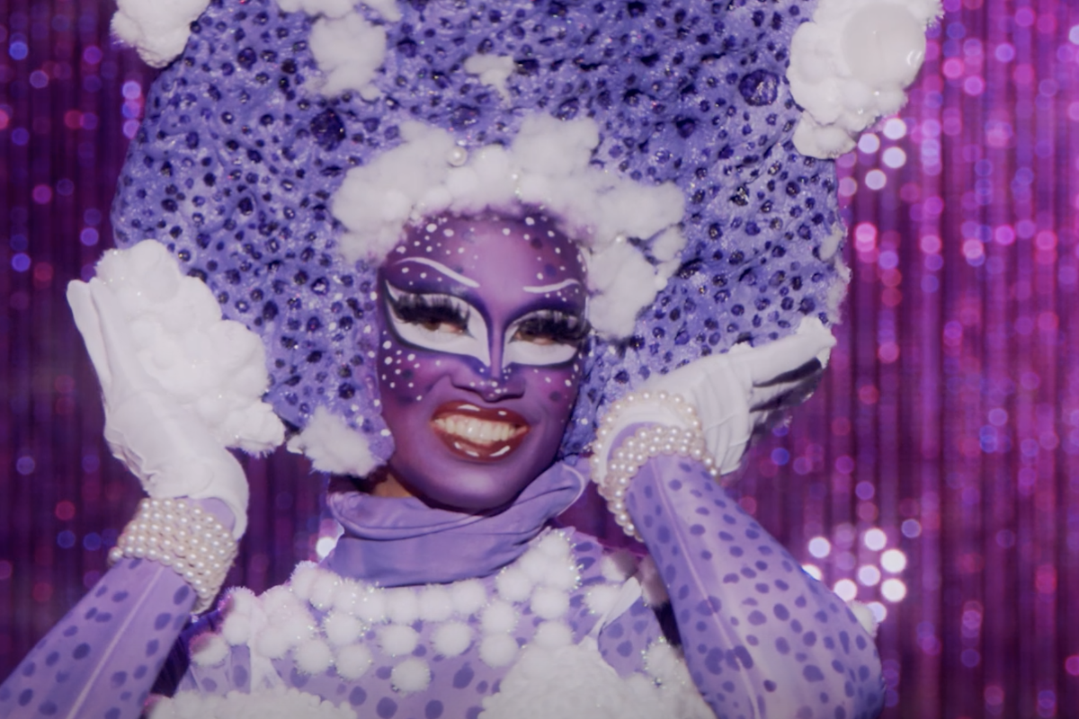 A drag queen in a purple outfit and face paint.