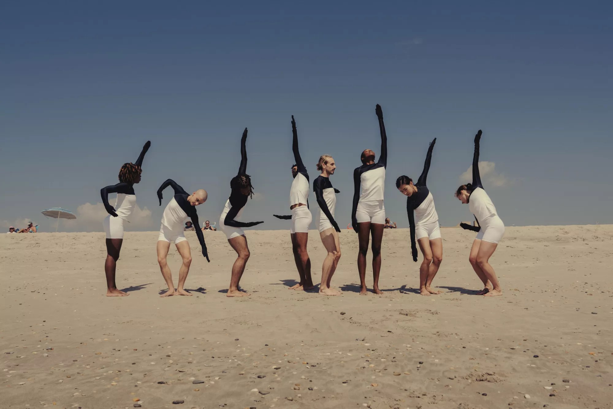 dancers in pose on a beach in white shirts and shorts with arms and hands covered in black cloth