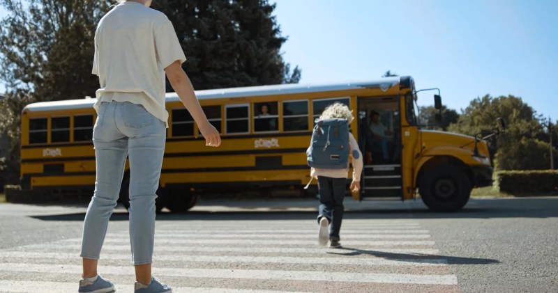 Stock photo of a mother watching a child crossing the street to board a yellow school bus