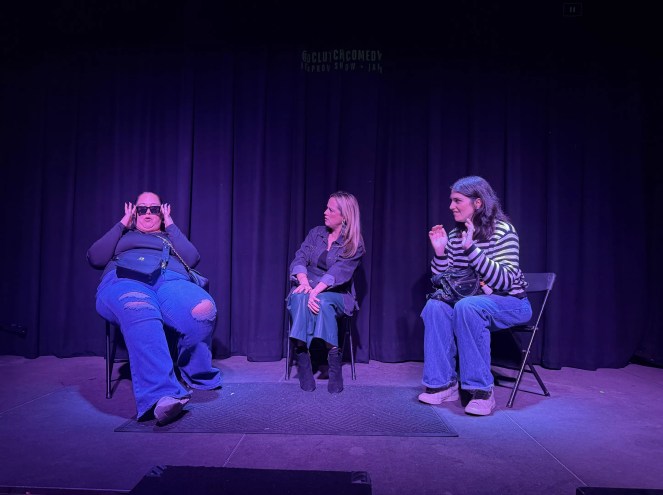 three women sit in chairs in front of a curtain on stage