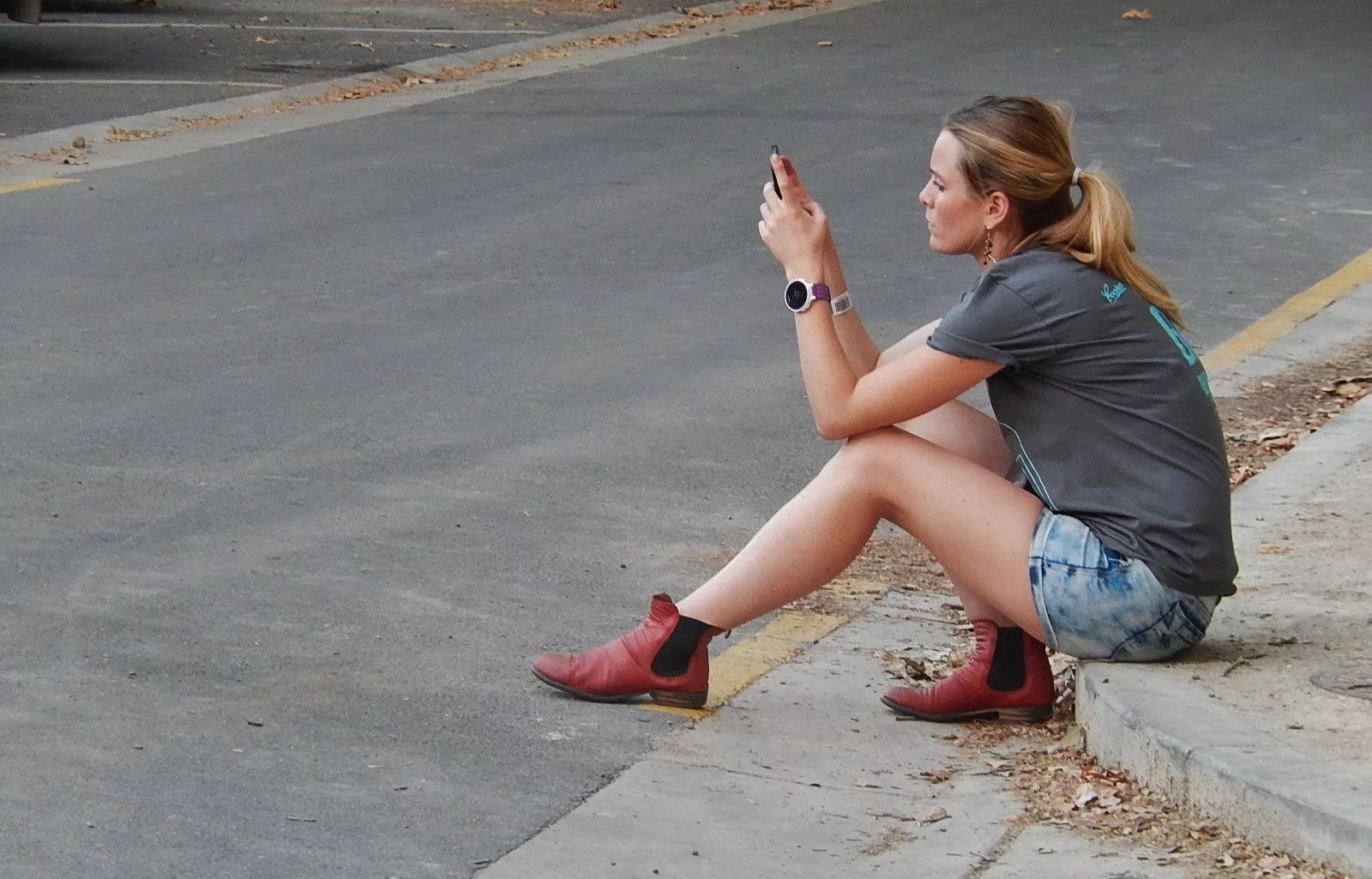 woman sits on a curb reading a text message