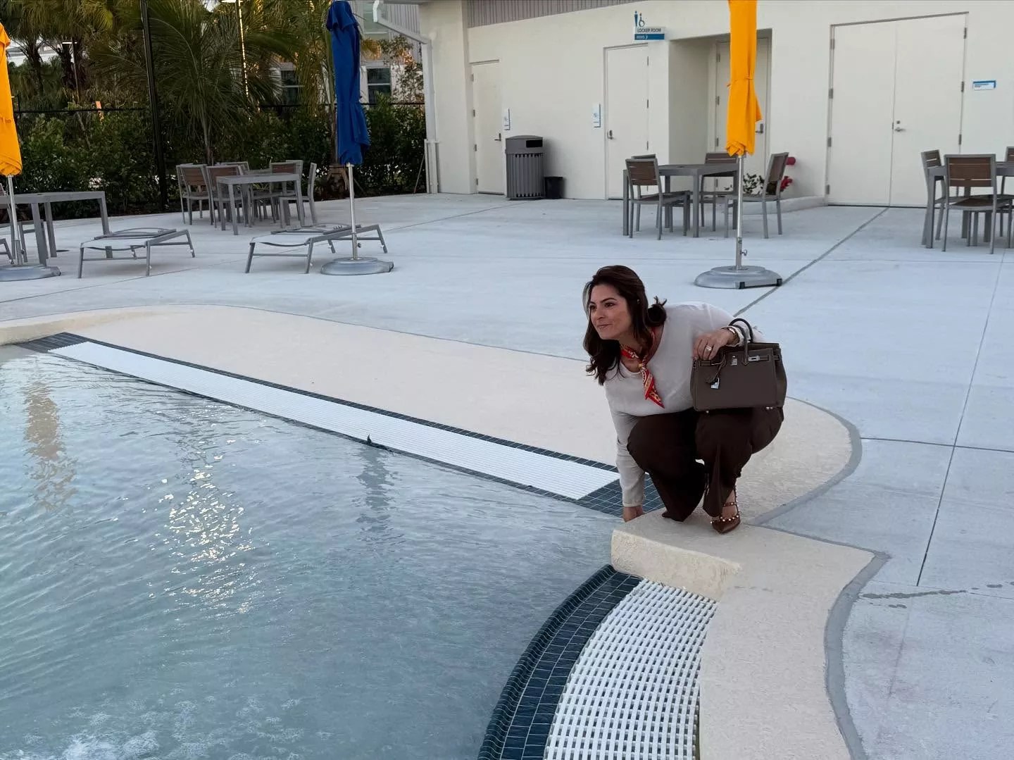 Christi Fraga bends down to touch the temperature of the pool holding her Birkin bag