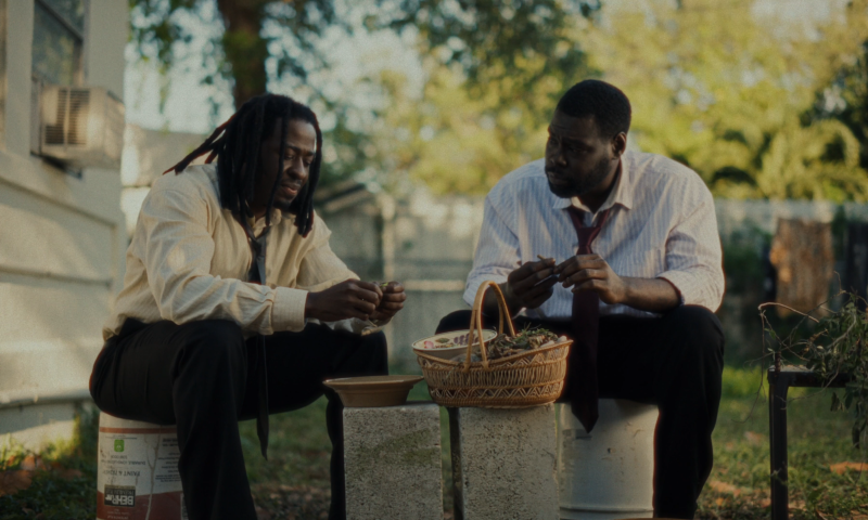 two men sit on buckets in a yard making a basket