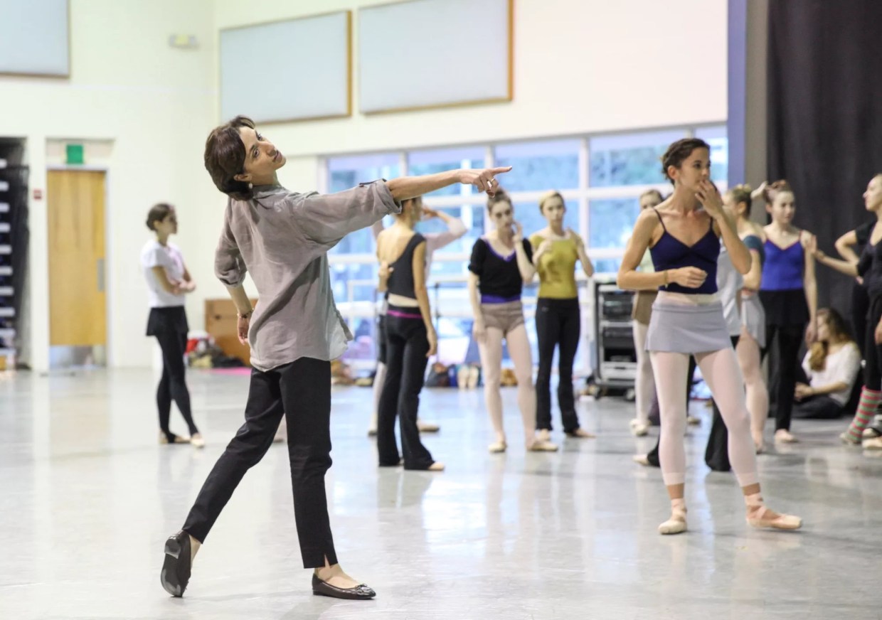 a ballet teacher poses in front of a class of students
