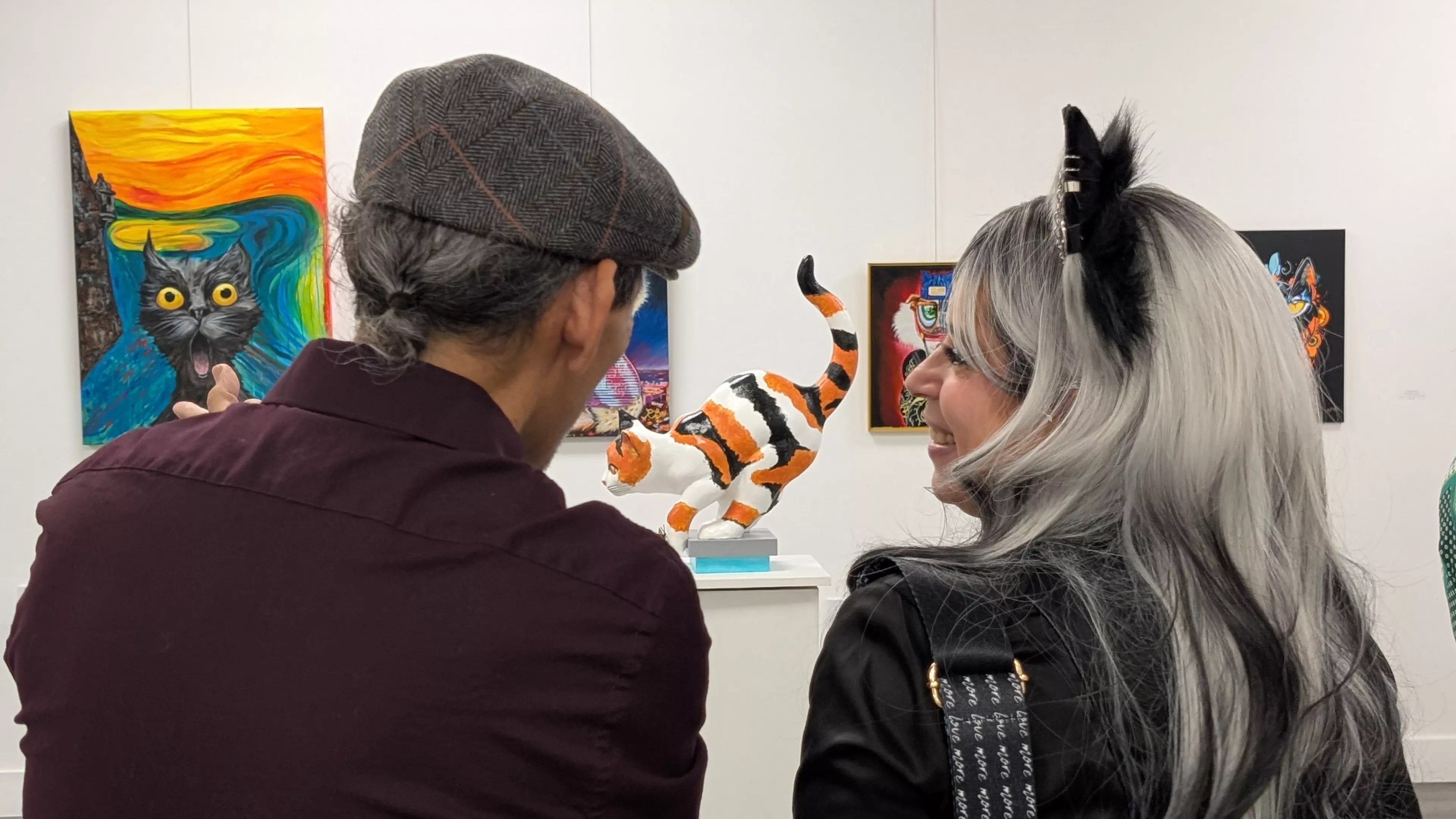 two people look at a sculpture of a cat inside a gallery