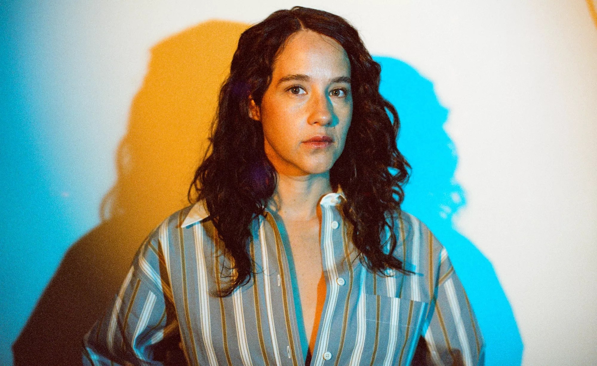 photo of a woman in a striped button down shirt against a vaguely psychedelic background