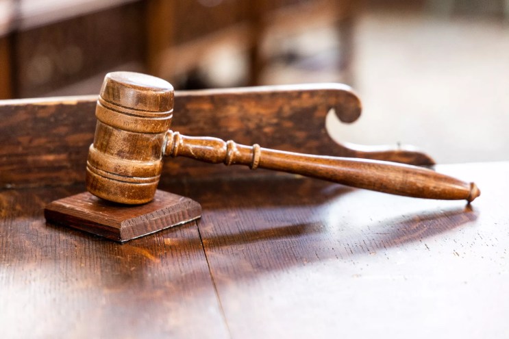 A judge's gavel sits on a wooden desk in a courtroom.