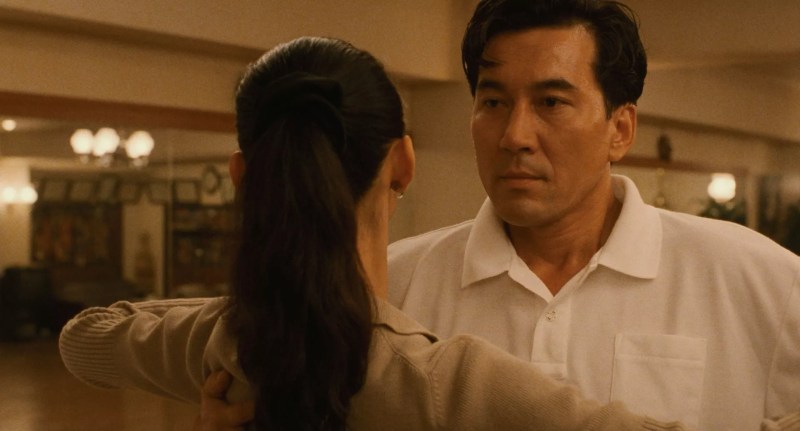 film still from Masayuki Suo's Shall We Dance? shows a closeup of actor Kōji Yakusho speaking to a woman with her back to the viewer