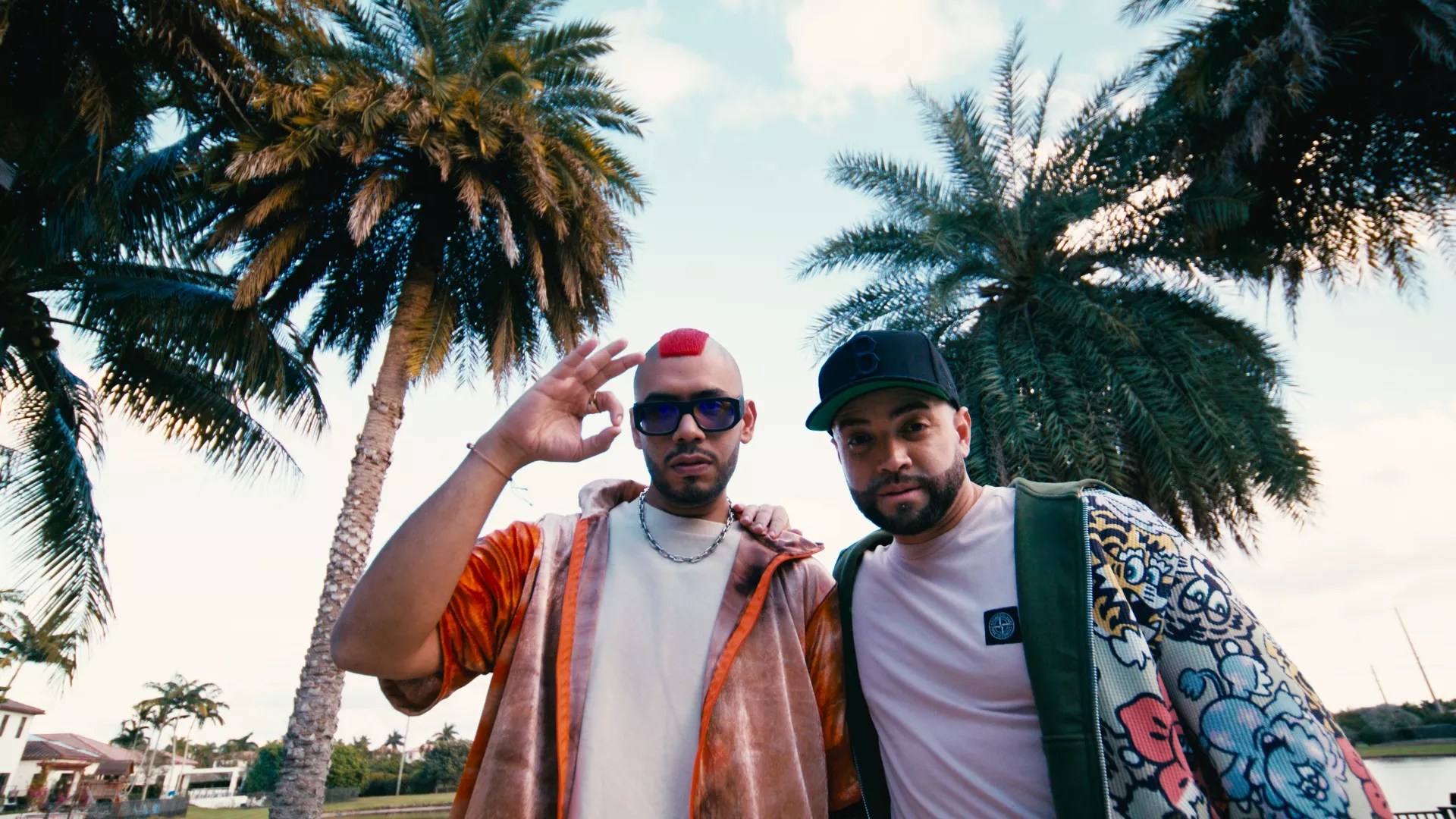 Two men posing with palm trees in the background.