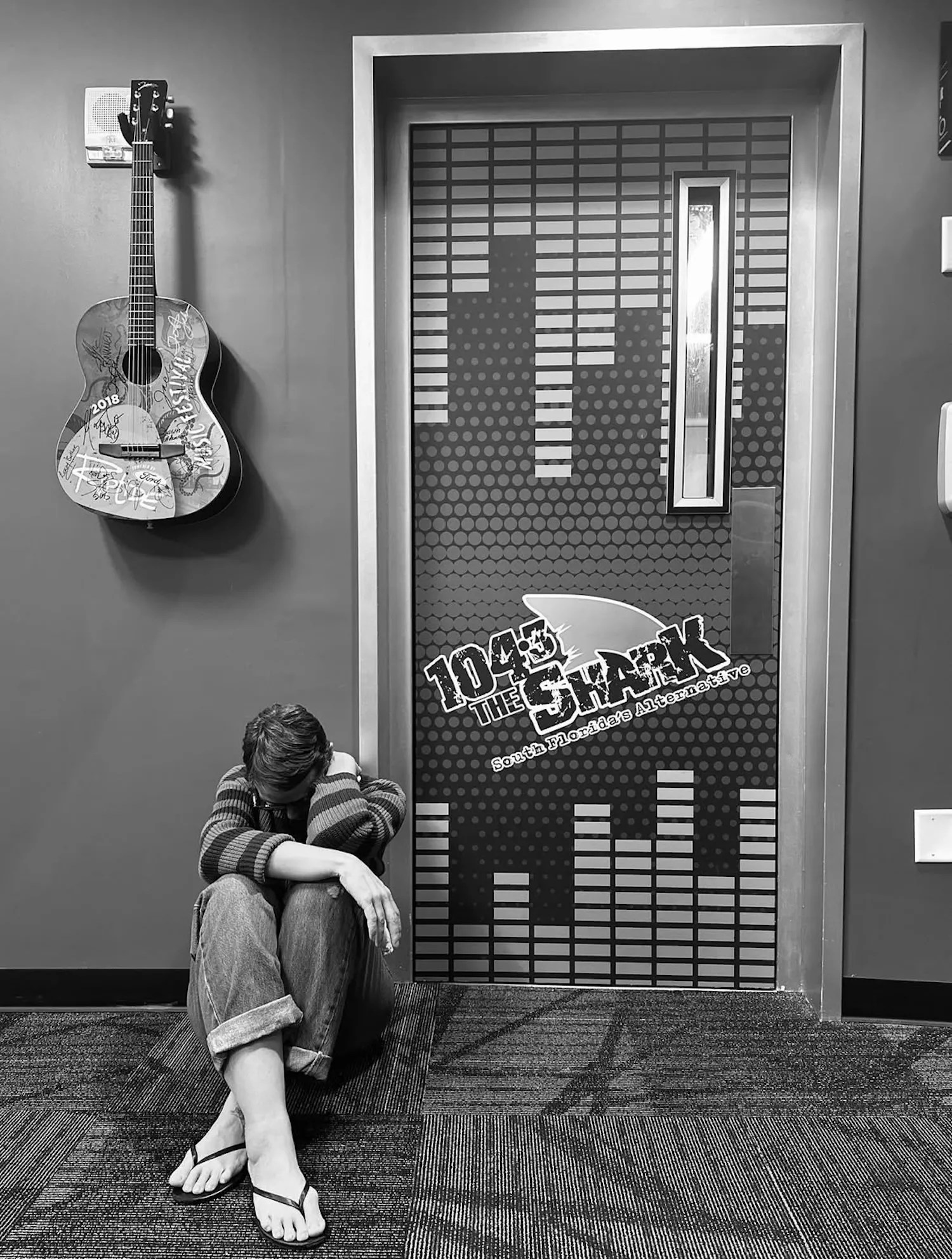 A woman sitting by a door outside a radio station