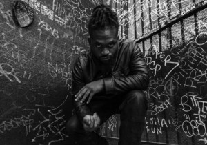 black and white picture of a young man by a graffiti-covered wall.