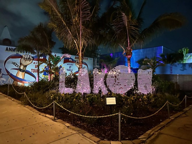 Picture of a sign in between palm trees at night